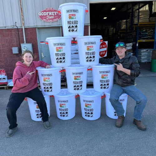 Roger's staff in front of a stack of feed buckets formed in a pyramid