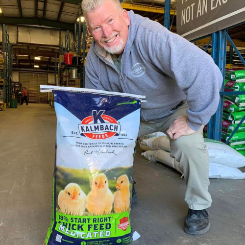 Roger's staff squatting behind a bag of chicken feed inside of the store