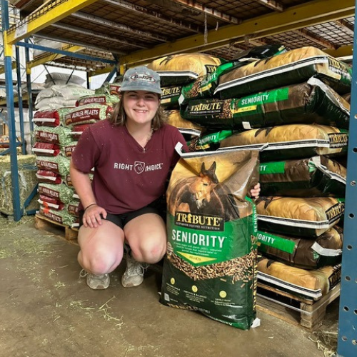 Roger's staff squatting beside a bag of horse feed inside of the store