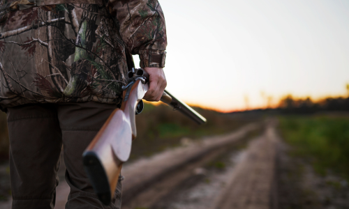 An hunter holding a shotgun wearing camo